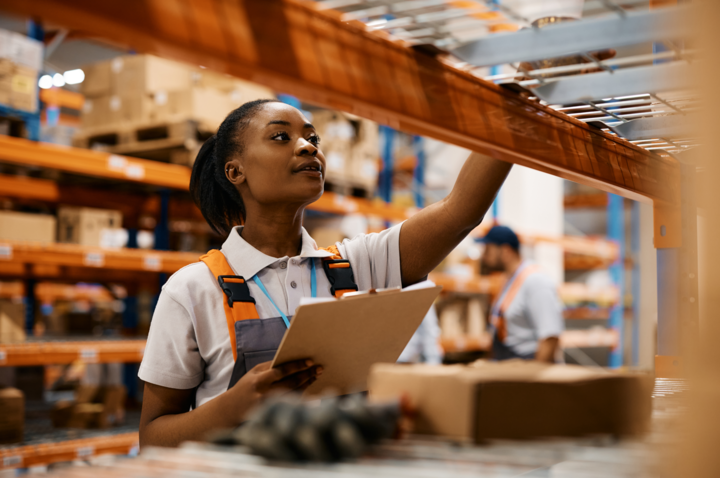 African American female worker checking inventory on shelves of distribution warehouse